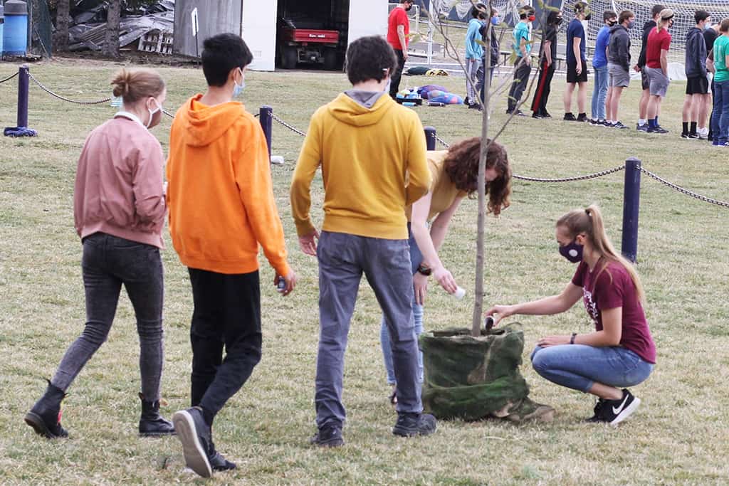 students help plant a tree during an outdoor chapel service
