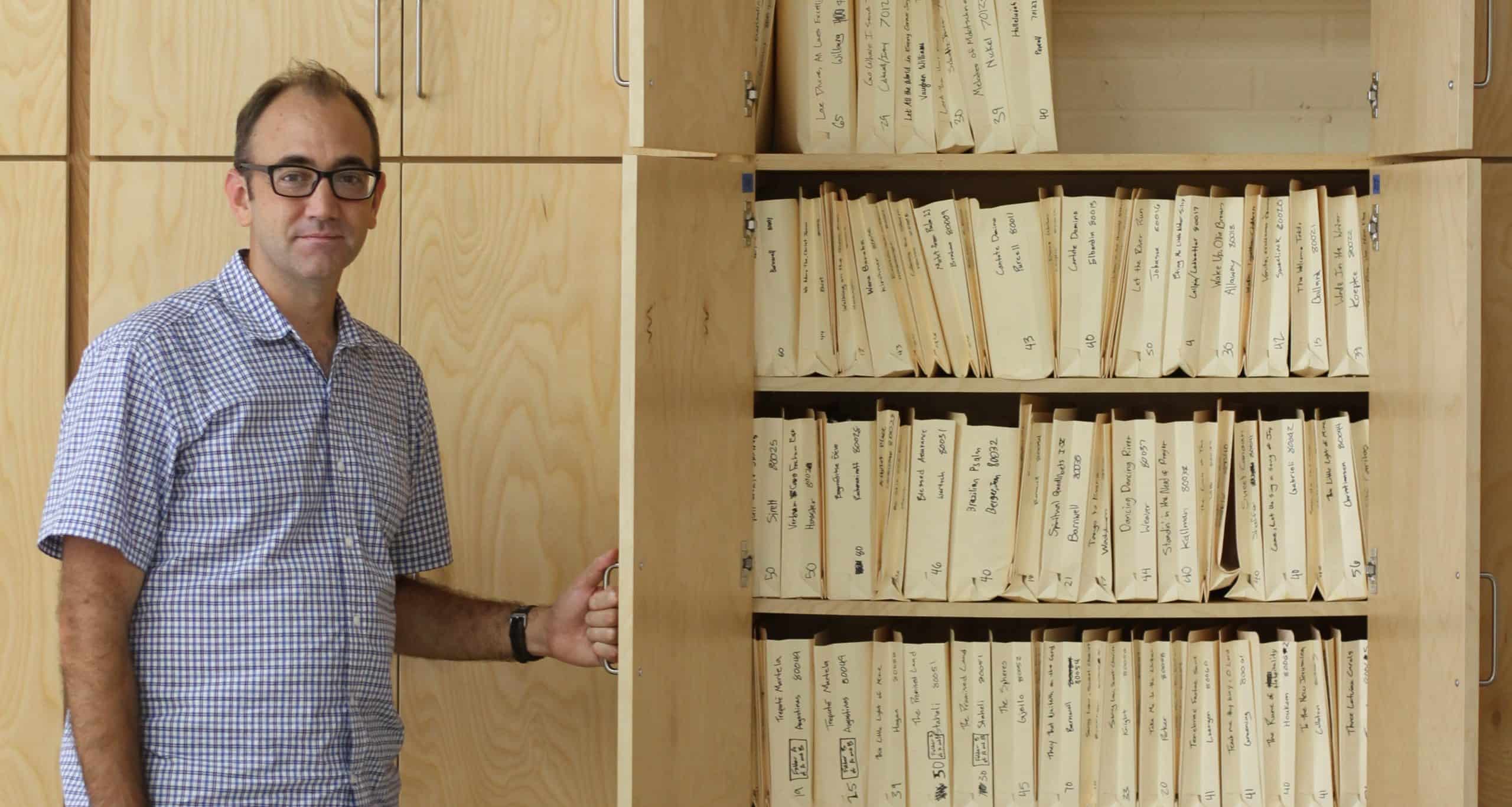 Jared Stutzman, choral director, with one small section of the choral music library of  more than 1,700 pieces, in new shelving